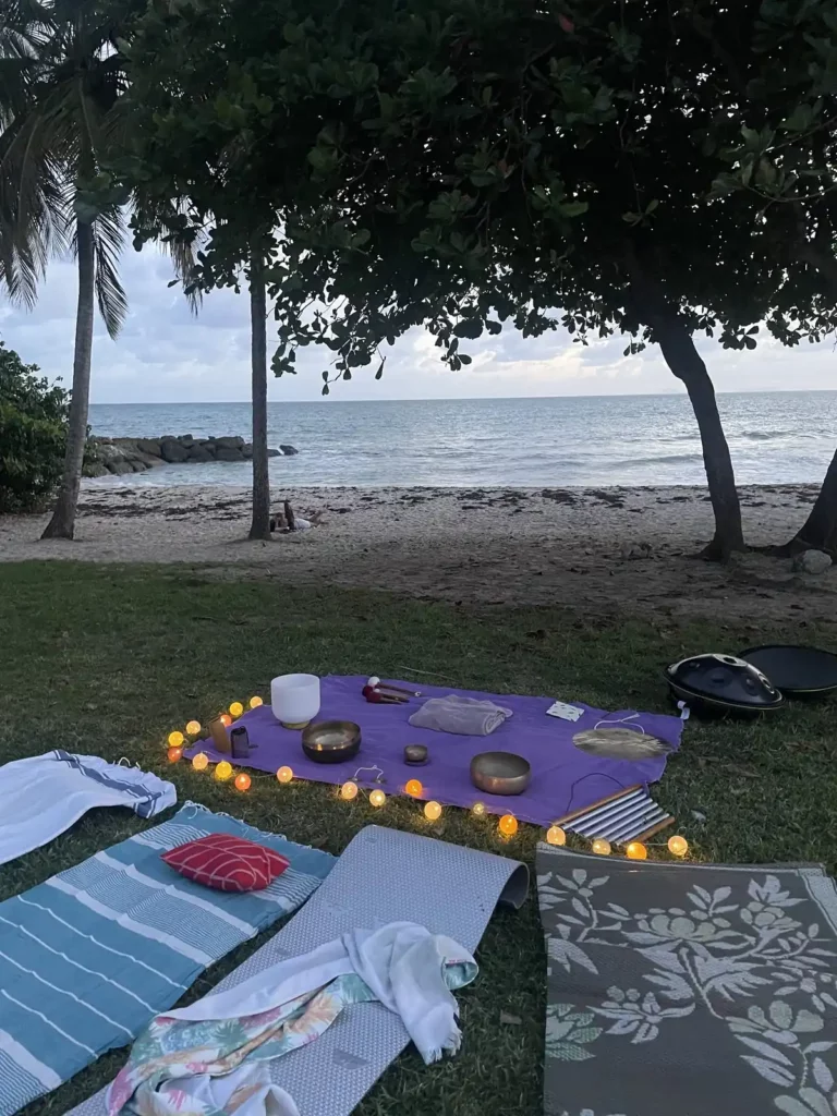 Bols chantants et bougies en cercle sur la plage au coucher du soleil, avec des tapis pour les participants